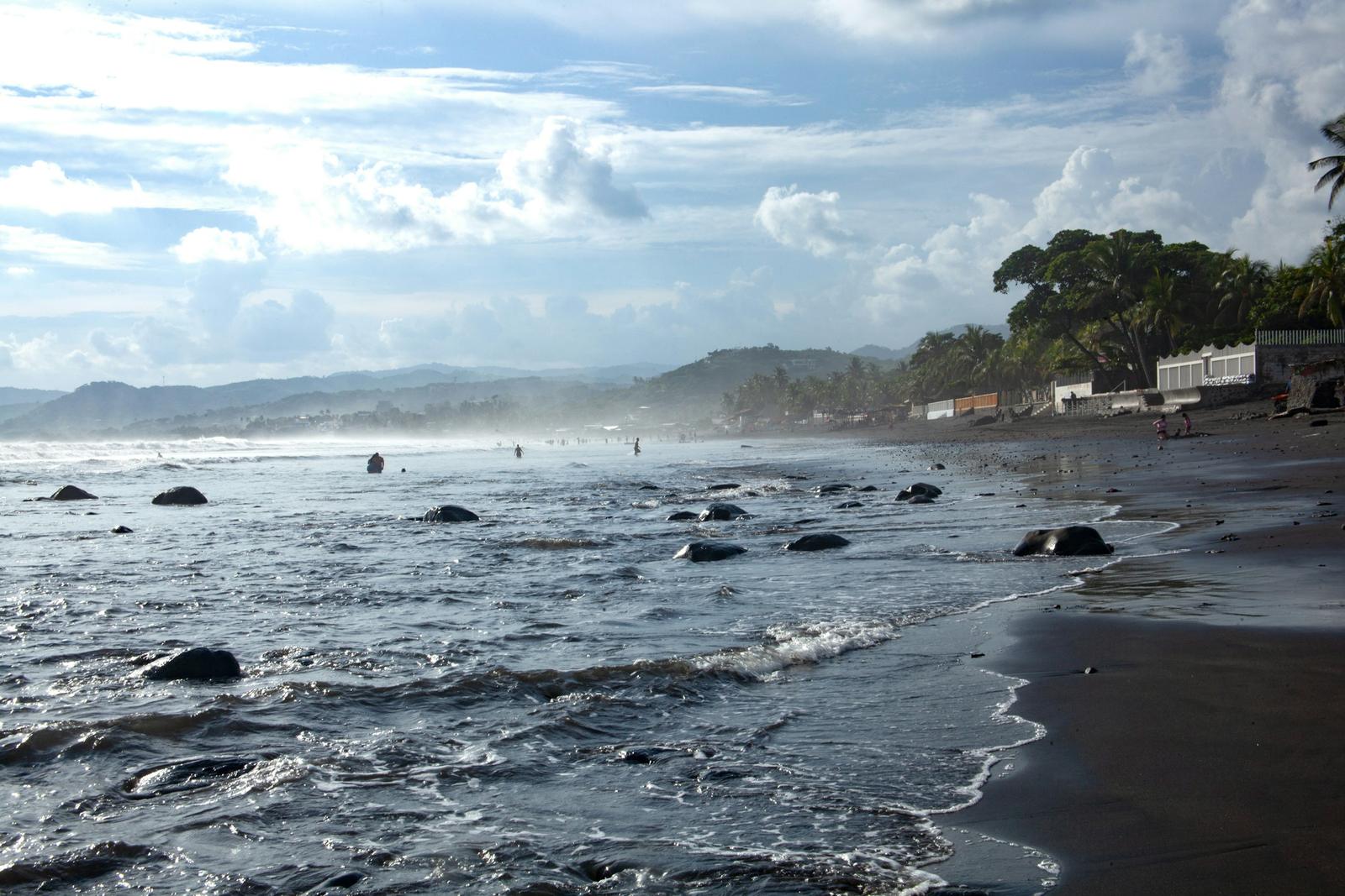 La orilla de Playa San Blas con bruma sobre el mar, palmeras y gente en el agua